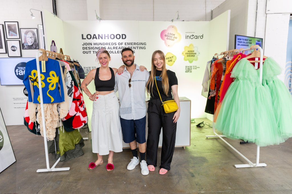 Three students smiling together with fashion garments hanging on racks 