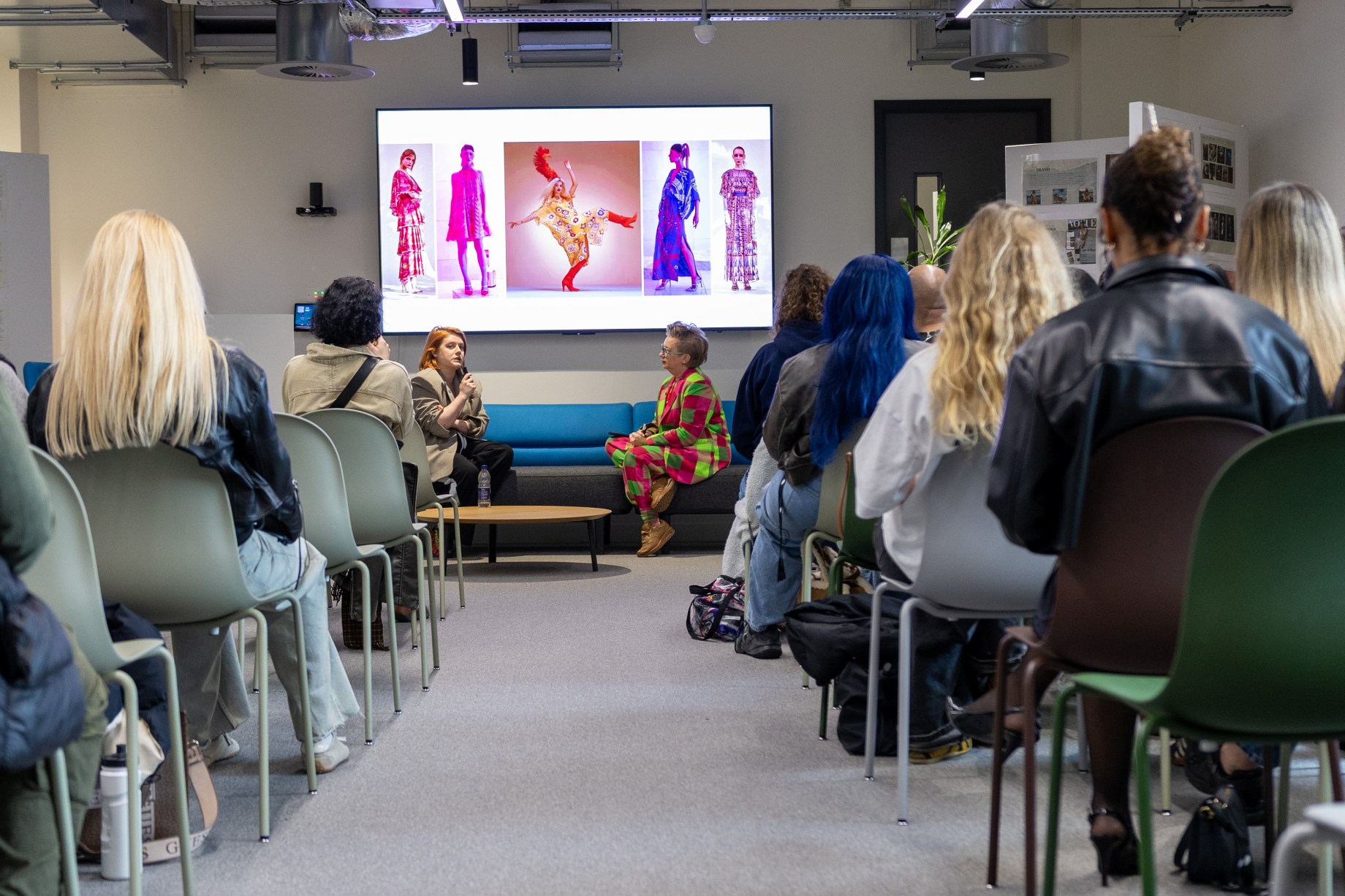 people in a room watching 2 people engage in a conversation