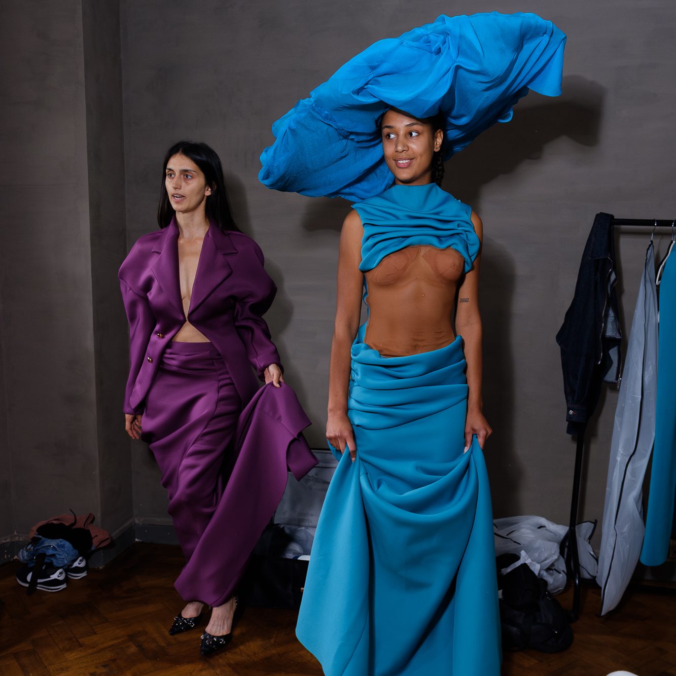 Two models in a purple and blue garment with large hat posing for editorial photos