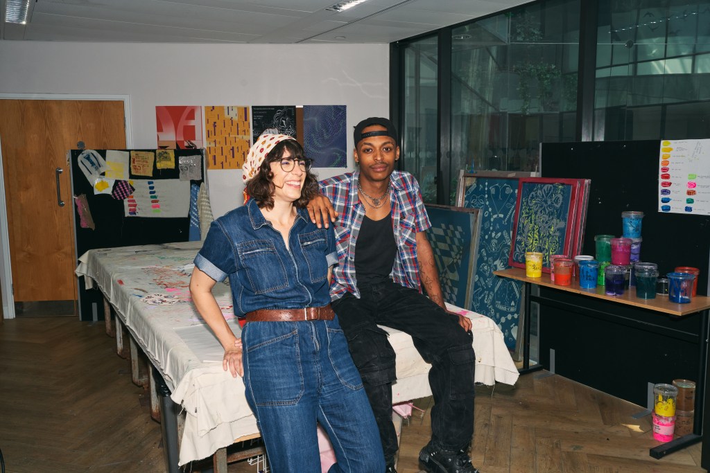 2 people sitting in room of painting and graphic design artwork made by students