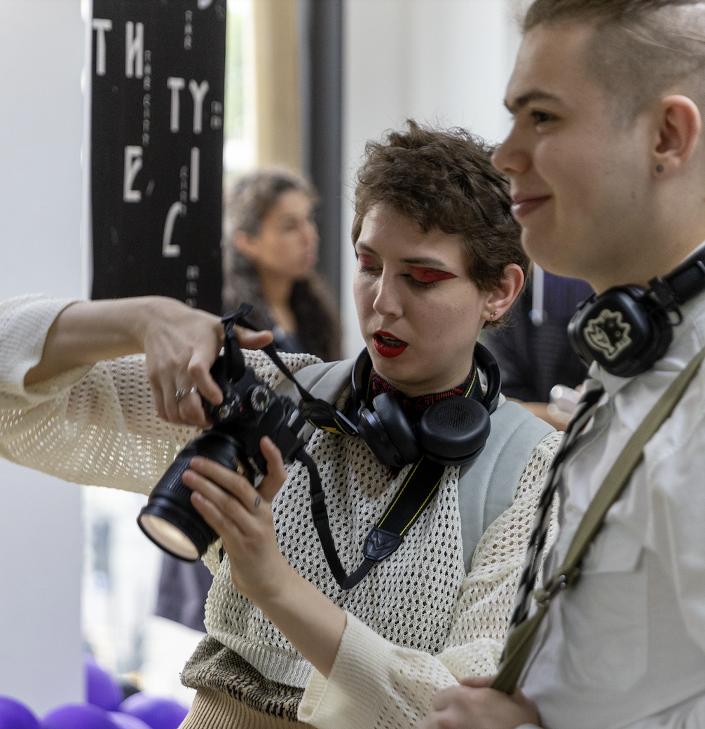 Student in an exhibition taking photos of her peers holding a camera
