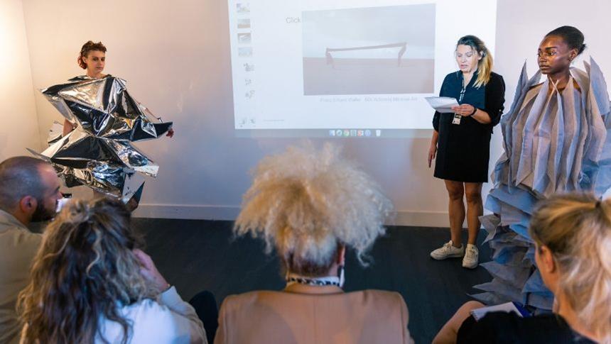An LCCA student presenting their work to people with 2 models