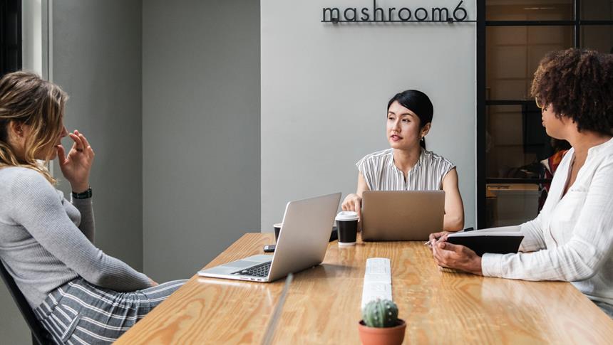 3 people sitting at table with laptops and notepads