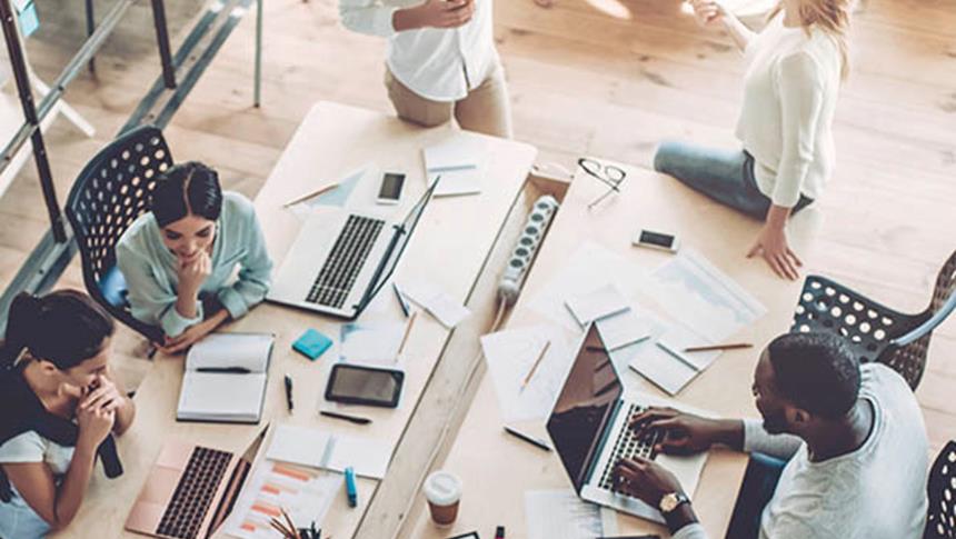 a desk with laptops and people sitting around it